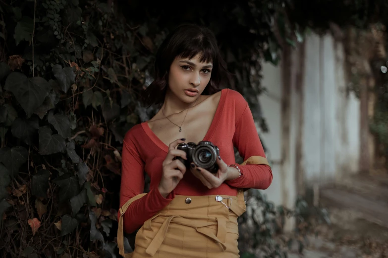 a woman standing next to a wall holding a camera, wearing a red outfit, wearing crop top and miniskirt, short brown hair and large eyes, today\'s featured photograph 4k