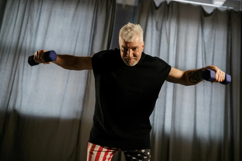 a man holding two dumbbells in front of a curtain, a portrait, inspired by Graham Forsythe, unsplash, hyperrealism, uncle sam, a silver haired mad, wearing a tee shirt and combats, [ theatrical ]