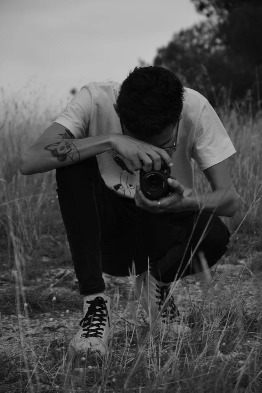 a man kneeling in a field holding a camera, a black and white photo, by Alexis Grimou, xxxtentacion, profile pic, deteriorated, headshot profile picture