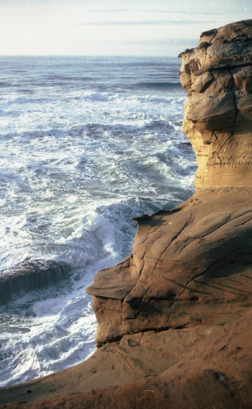 a man standing on top of a cliff next to the ocean, sandstone, turbulent waves, pareidolia, slide show