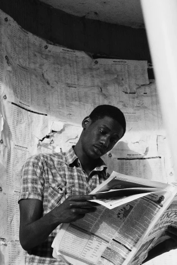 a black and white photo of a man reading a newspaper, by Robert Feke, african man, around 1 9 years old, hanging, studious