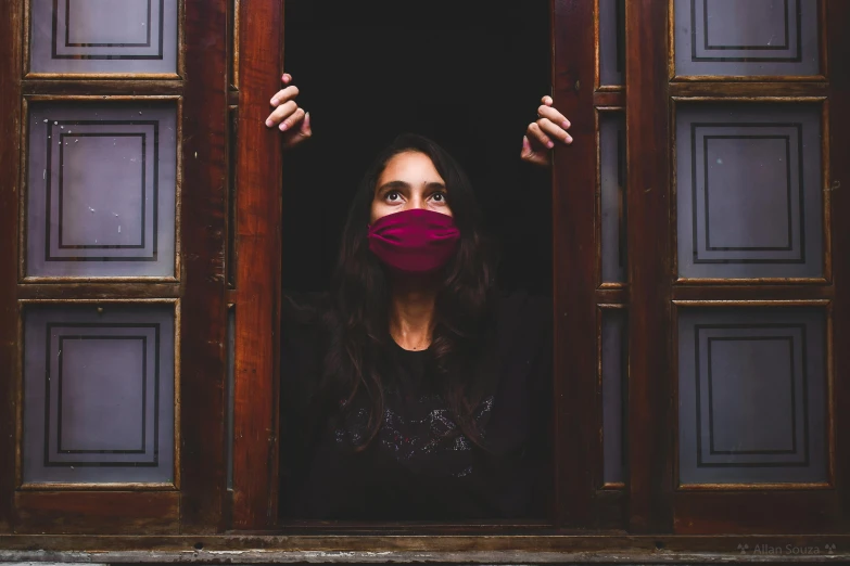 a woman wearing a face mask looking out a window, a portrait, pexels contest winner, about to enter doorframe, glowing magenta face, a wooden, hostages
