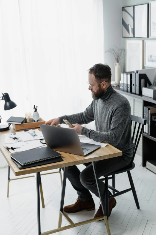 a man sitting at a desk working on a laptop, curated collections, selling insurance, papers on table, gray men