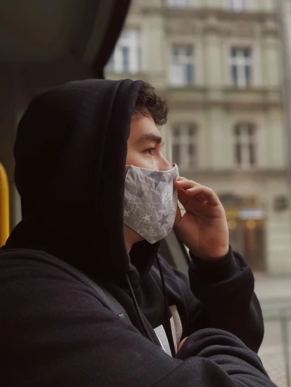 a man wearing a face mask while talking on a cell phone, by Adam Marczyński, pexels contest winner, gray hoodie, 🚿🗝📝, profile image, thoughtful pose