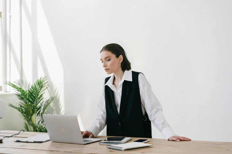 a woman sitting at a desk in front of a laptop computer, by Carey Morris, trending on pexels, technical vest, elegant regal posture, on a white table, aleksander rostov