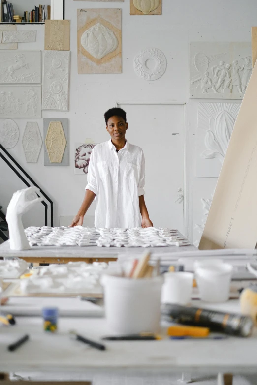 a woman that is standing in front of a table, a marble sculpture, process art, white ceramic shapes, modeling studio, maria borges, an architectural