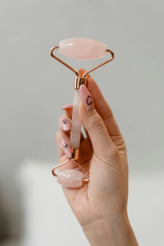 a woman holding a rose quartz facial roller, floating symbols and crystals, curved blades on each hand, top angle, date