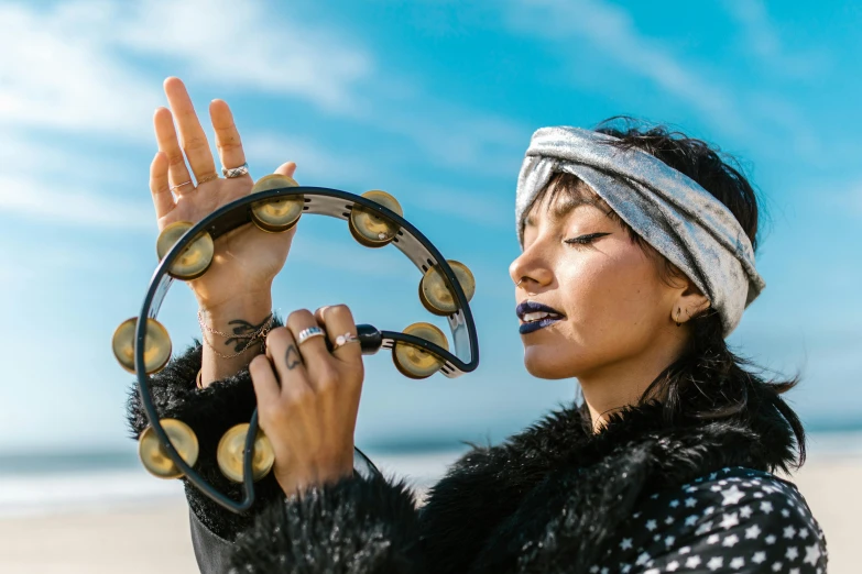 a woman standing on top of a beach holding a tambour, trending on pexels, kinetic art, septum piercing, wearing two metallic rings, band playing instruments, moroccan queens ny