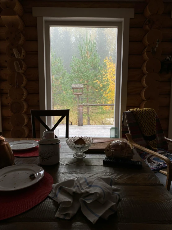 a table that has plates on it in front of a window, by Jaakko Mattila, foggy day outside, breakfast, cabin, low quality photo