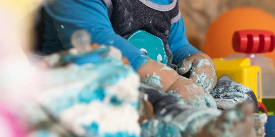 a close up of a child playing with toys, by Helen Stevenson, pexels, process art, baking a cake, blue paint on top, sitting in his highchair, chalky