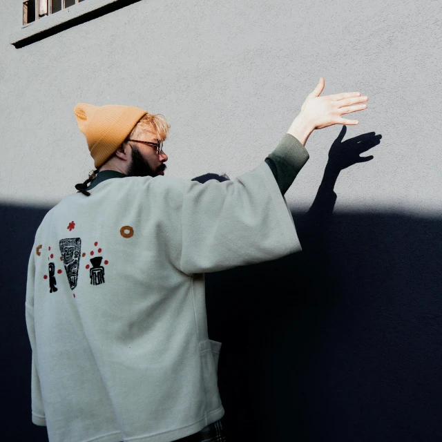 a man that is standing in front of a wall, unsplash, graffiti, waving robe movement, ginger bearded man with glasses, uniform off - white sky, back light