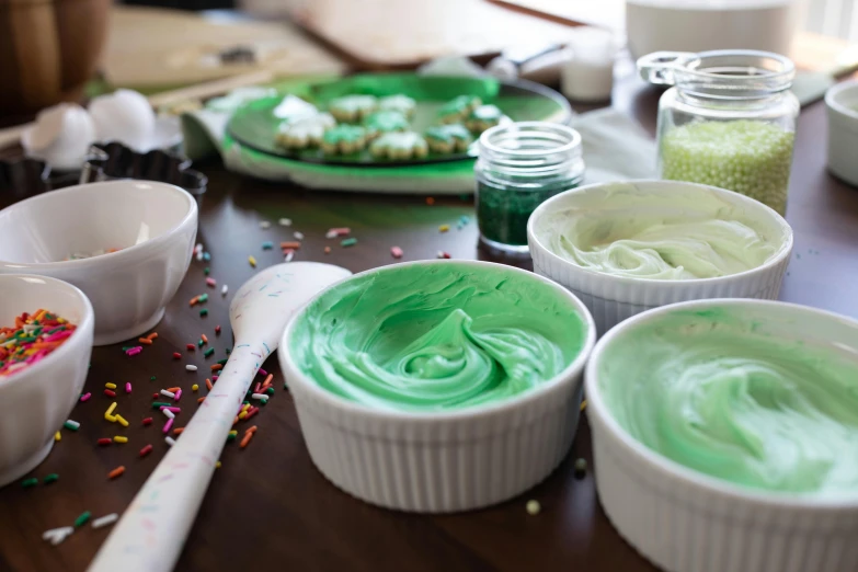 a table topped with bowls filled with green frosting, paints mixing, arney freyag, background image, medium level shot