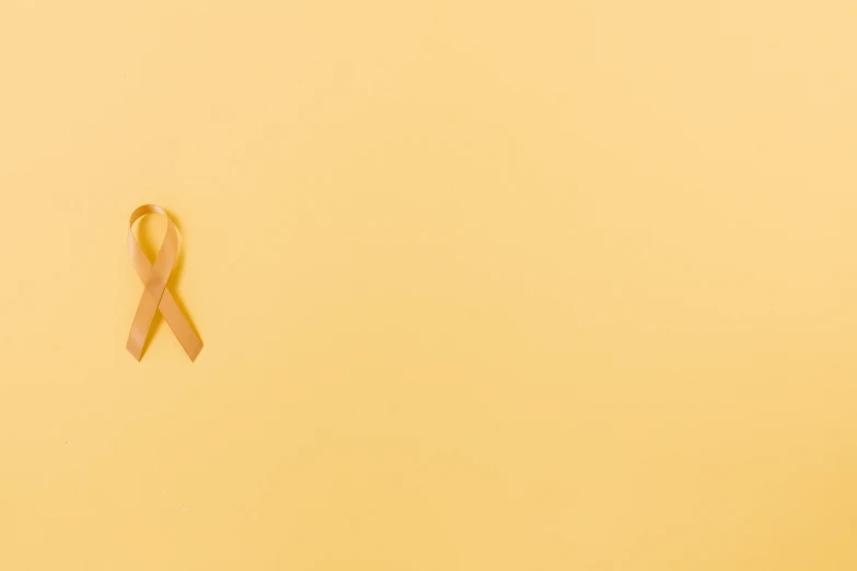a yellow ribbon on a yellow background, a picture, by Gavin Hamilton, pexels contest winner, background image, tumors, light brown background, 2 2 years old