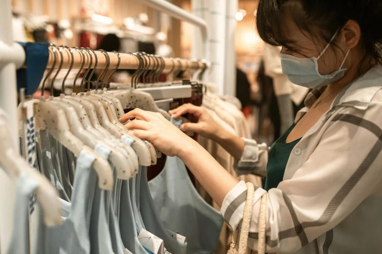 a woman wearing a face mask in a clothing store, a photo, trending on pexels, thumbnail, white and teal garment, cardboard, small details