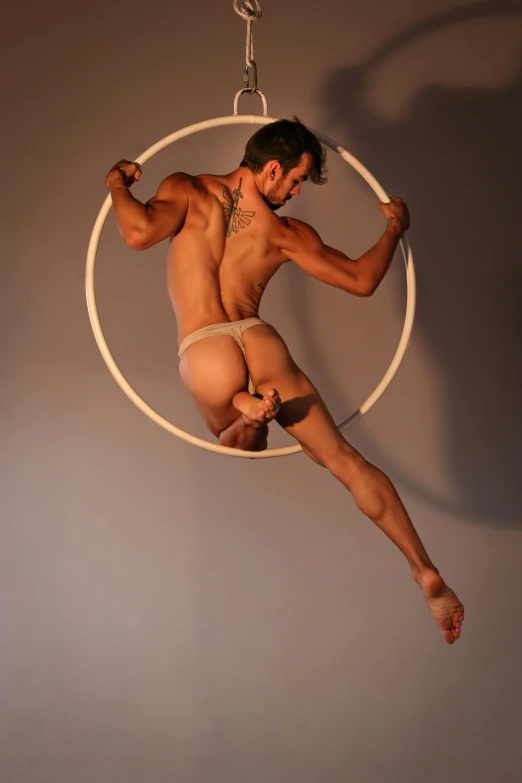 a man that is in the air with a hoop, an album cover, inspired by Roberto Ferri, arabesque, slide show, male model, bum, high angle shot