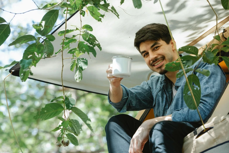 a man sitting on a bench holding a glass of water, inspired by Adam Dario Keel, pexels contest winner, art nouveau, in a tree house, attractive man drinking coffee, desert white greenhouse, ginko showing a new mushi