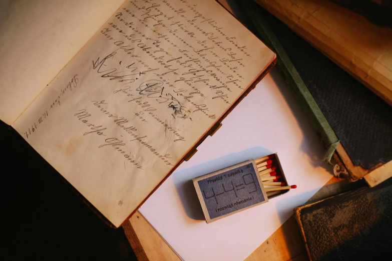 an open book sitting on top of a table next to a matchstick, a sketch, pexels contest winner, old scientific documents, first aid kit, signatures, 1 9 th century photography