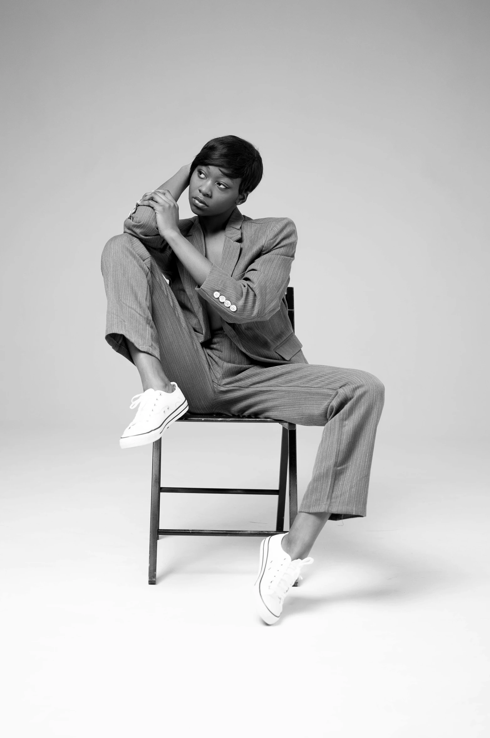 a black and white photo of a man sitting on a chair, naomi campbell, androgynous person, wearing a track suit, doing an elegant pose over you