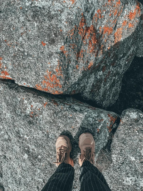 a person standing on top of a large rock, whole shoe is in picture, dark grey and orange colours, high view, ((rocks))