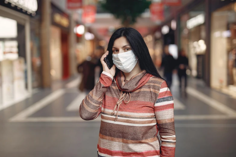 a woman wearing a face mask while talking on a cell phone, trending on pexels, mall background, brown, romanian, disease