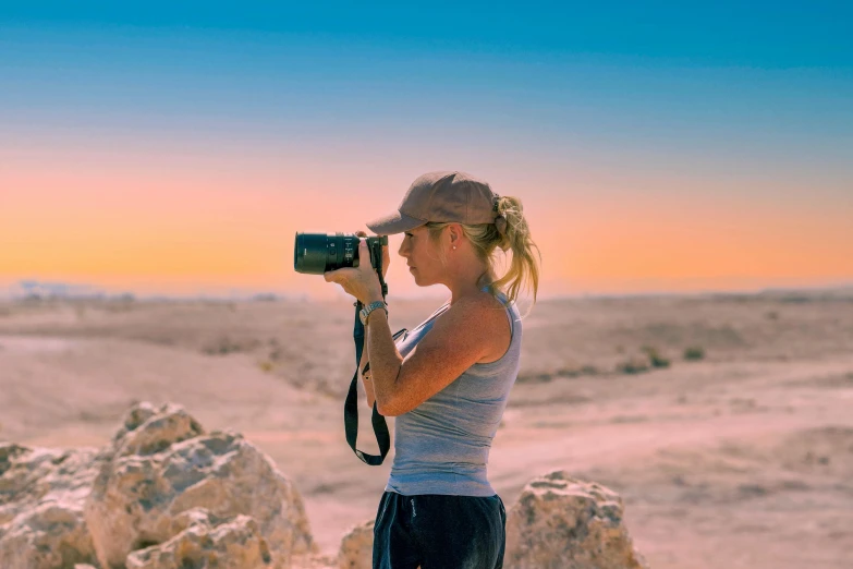 a woman taking a picture with a camera in the desert, pexels contest winner, athlete photography, profile image, the australian desert, warm glow