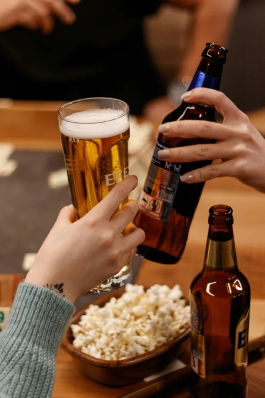 a couple of people sitting at a table with beer and popcorn, by Everett Warner, pexels contest winner, beer bottle, pouring, close up details, holding an epée