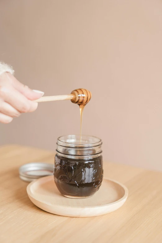 a person holding a wooden stick over a jar of honey, by Julia Pishtar, sitting on a mocha-colored table, detailed product image, vine, black