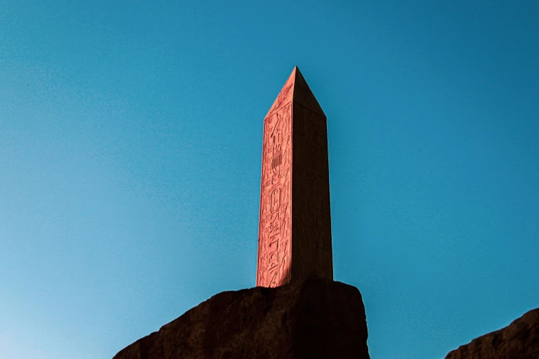 a tall obelisk sitting on top of a rock, by Attila Meszlenyi, postminimalism, red and blue back light, egyptian iconography, promo image, blue sky