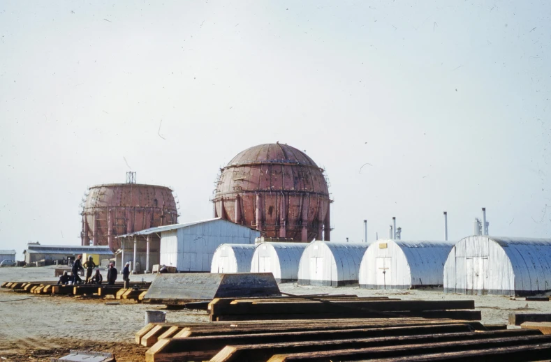 a group of tanks sitting next to each other on top of a dirt field, by Christo, gutai group, biroremediation plant, rounded roof, icbm, historic photograph