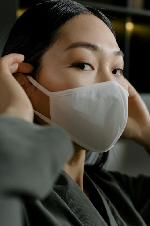 a woman wearing a face mask while sitting on a couch, inspired by Kanō Naizen, trending on pexels, renaissance, close up front view, ear, made of lab tissue, singapore