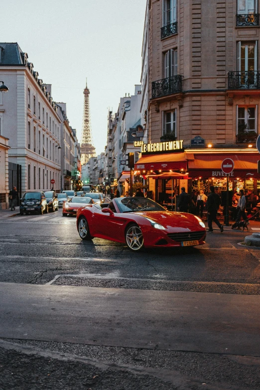 a red car driving down a street next to tall buildings, a photo, renaissance, with eiffel view, supercar, glowing street signs, french village exterior