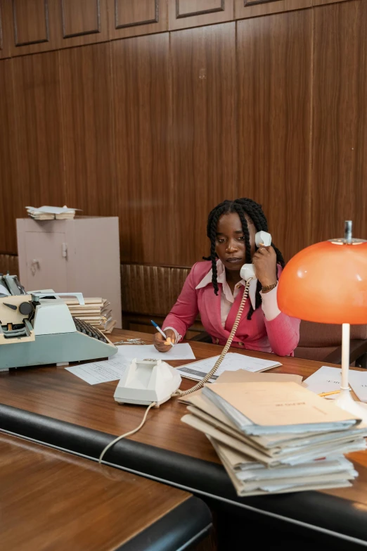 a woman sitting at a desk talking on a phone, an album cover, 2019 trending photo, live-action archival footage, set inside of the bank, maria borges