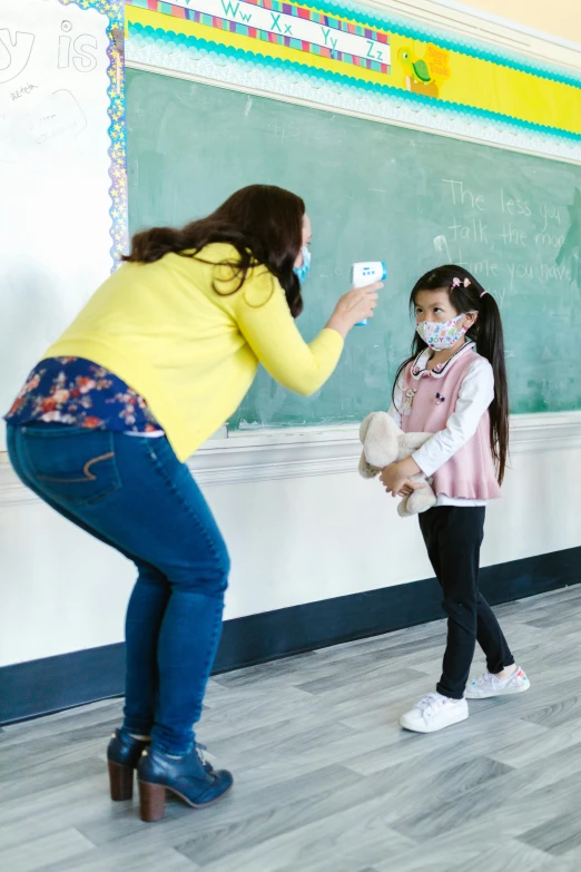 a woman standing next to a little girl in front of a blackboard, pexels contest winner, american barbizon school, masked person in corner, square, healthcare, hey buddy