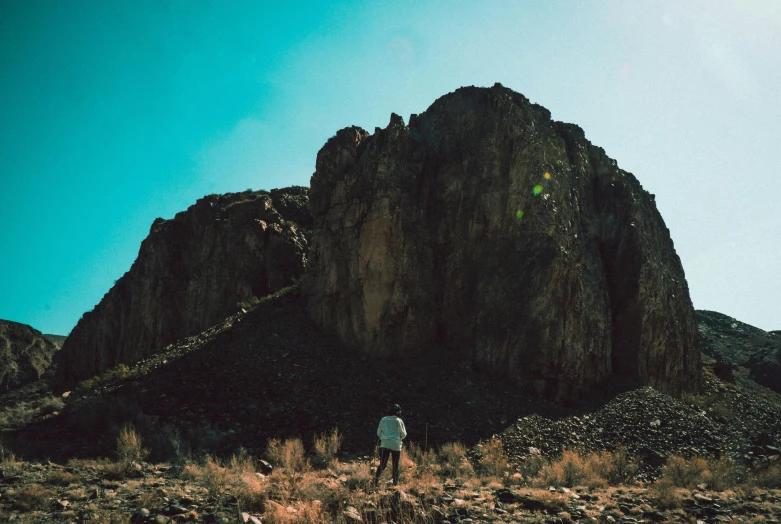 a person standing in front of a mountain, by Lee Loughridge, unsplash contest winner, visual art, black mesa, rocks flying, background image, walking away from the camera