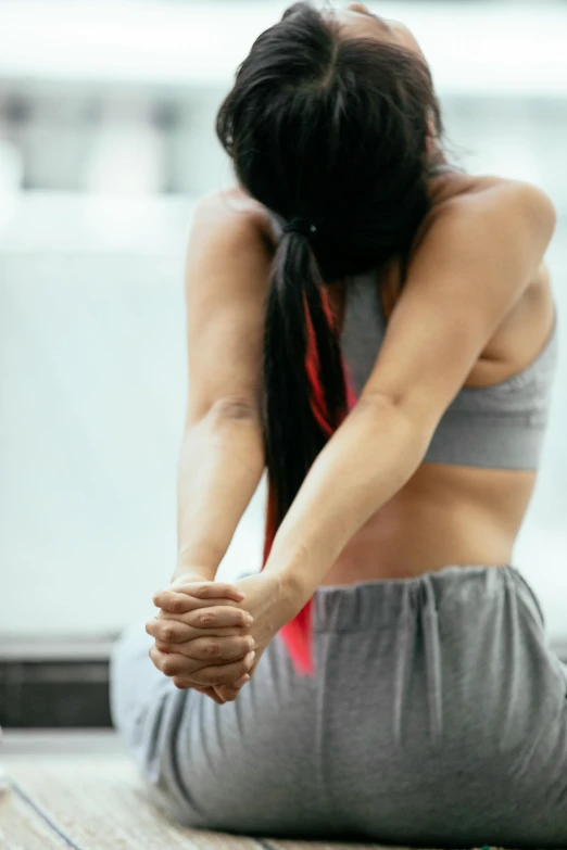 a woman sitting on the floor with her head in her hands, pexels contest winner, sport bra, closeup of arms, dynamic stretching, facing away from camera