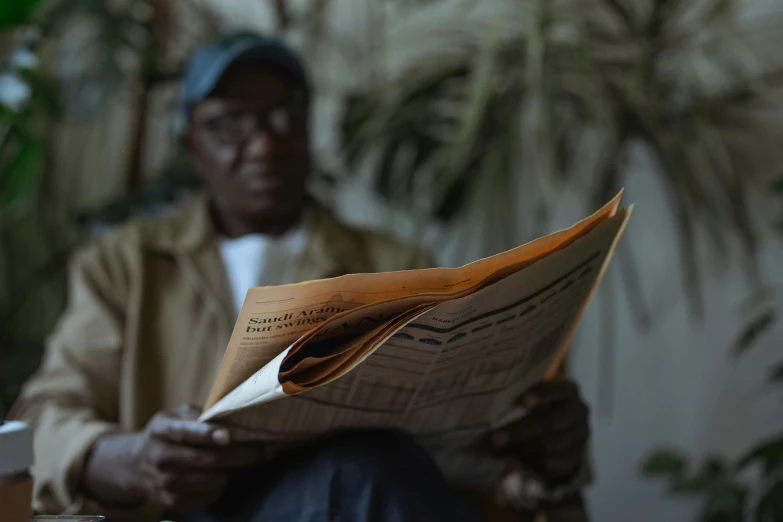 a man sitting in a chair reading a newspaper, by Carey Morris, pexels contest winner, man is with black skin, faded glow, ignant, shot on sony a 7