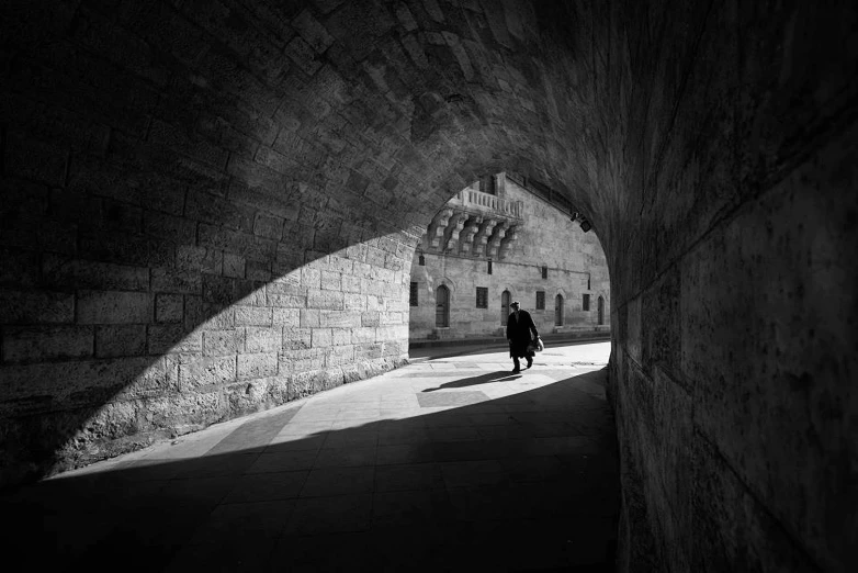 a black and white photo of a person walking through a tunnel, a black and white photo, by Constantine Andreou, city walls, andrey gordeev, jerusalem, hasselblad photography