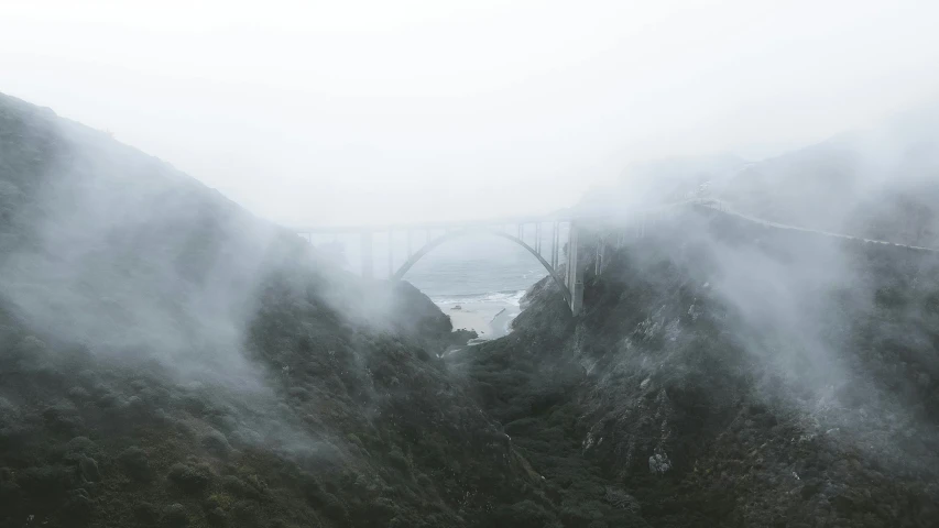 a train traveling over a bridge on a foggy day, pexels contest winner, romanticism, california coast, massive arch, gray wasteland, the middle of a valley