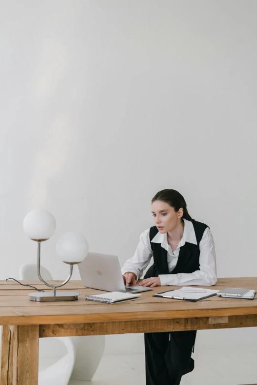 a woman sitting at a table working on a laptop, in a white room, light and dark, looking serious, - 9