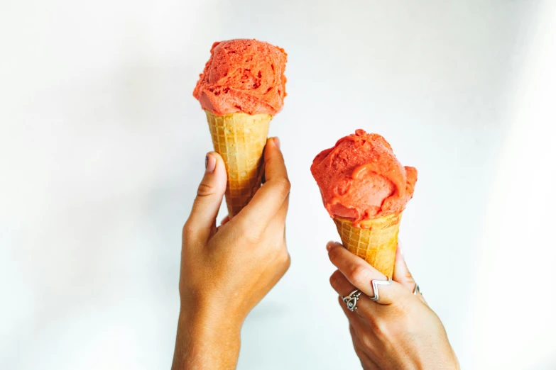 two people holding up two ice cream cones, by Emma Andijewska, pexels, coral red, lush, instagram post, edible