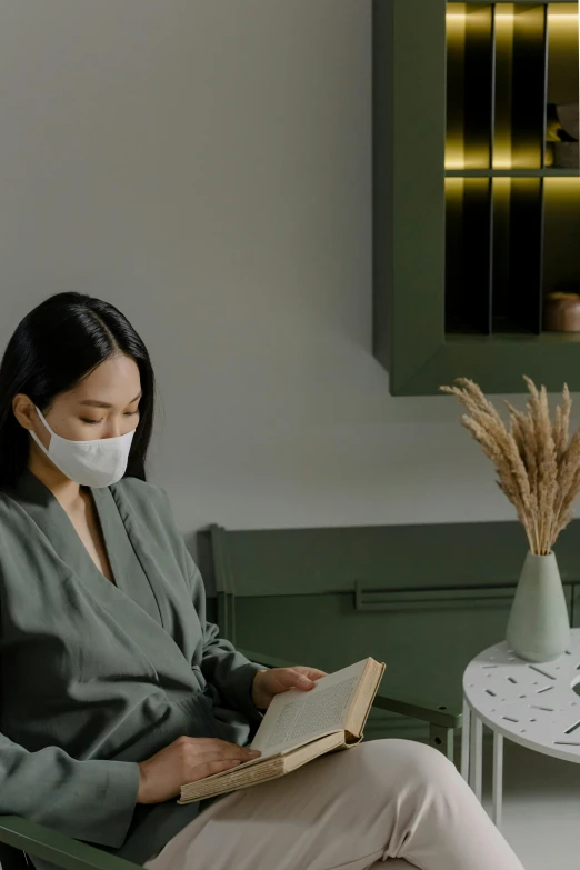 a woman sitting in a chair reading a book, inspired by Li Di, trending on pexels, surgical mask covering mouth, asian human, spa, reading nook