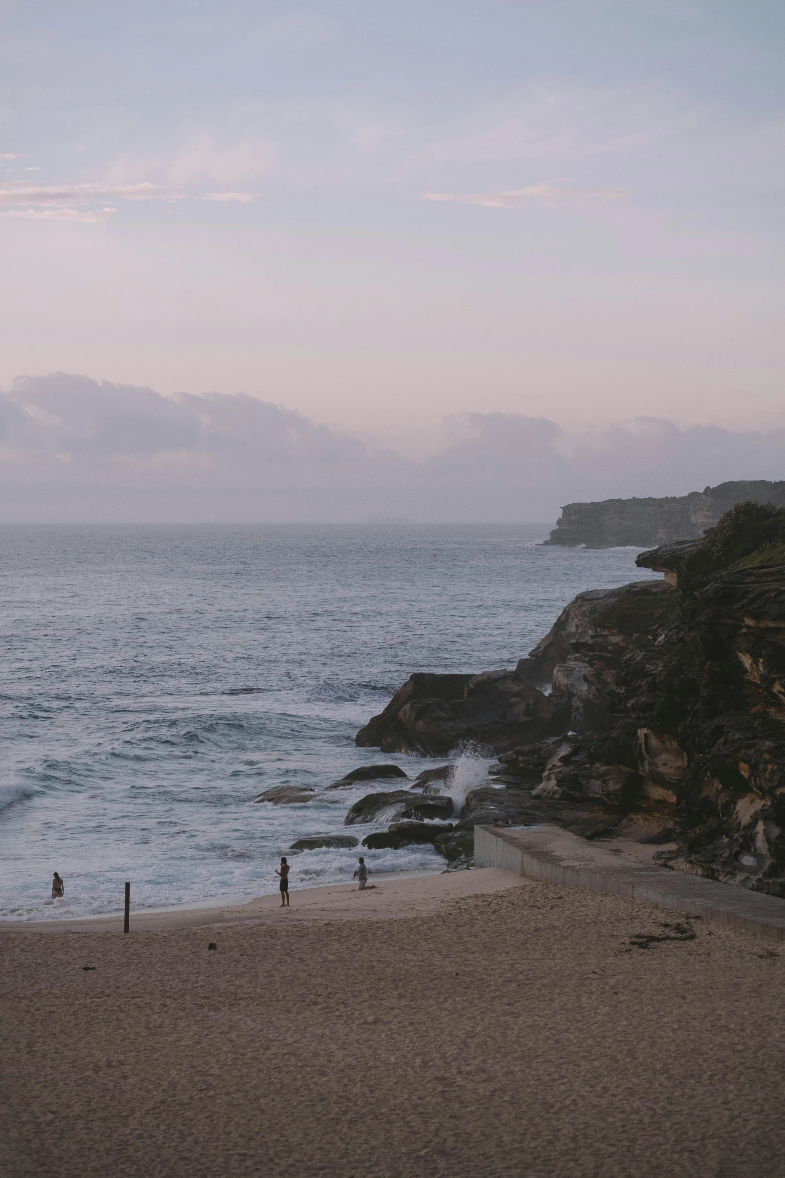 a couple of people standing on top of a sandy beach, cliff side at dusk, sydney, slight haze, no crop