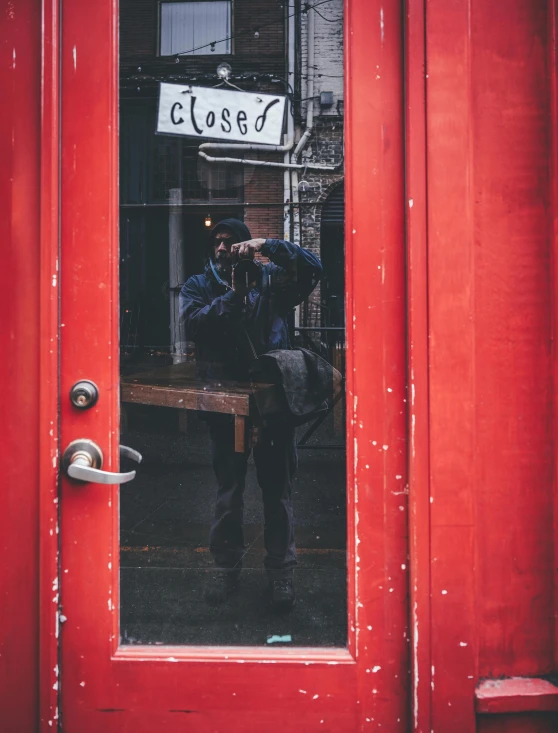 a man taking a picture of himself in the reflection of a red door, pexels contest winner, happening, small hipster coffee shop, & the eyes & mouth are closed, boarded up, cloese-up