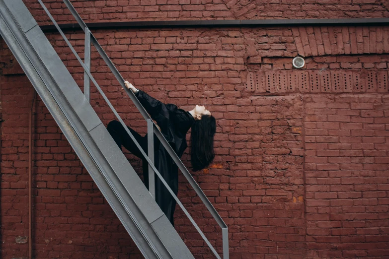 a woman climbing a set of stairs in front of a brick wall, an album cover, by Attila Meszlenyi, pexels contest winner, arabesque, wearing a black catsuit, 15081959 21121991 01012000 4k, contemporary dance poses, bridge