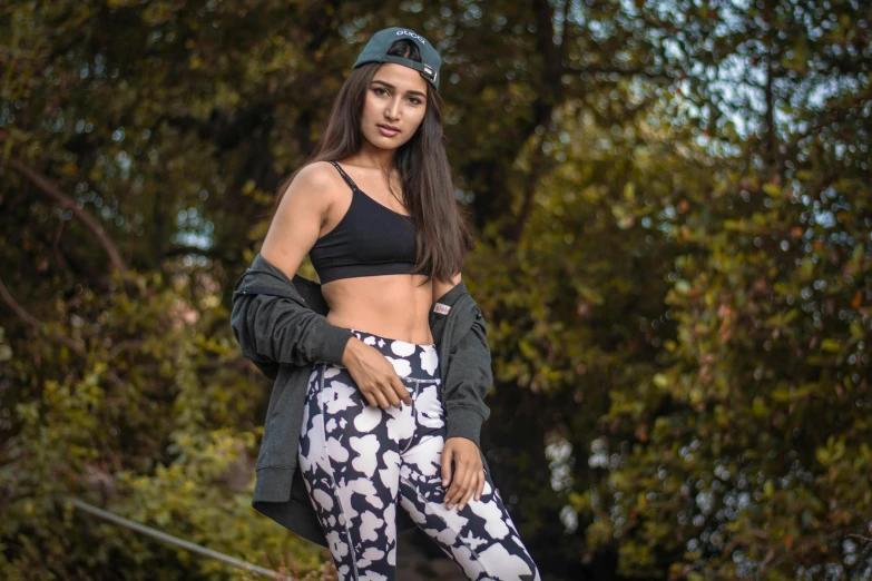 a beautiful young woman standing on top of a skateboard, a portrait, trending on pexels, graffiti, detailed sports bra, indian, black leggins, foliage clothing