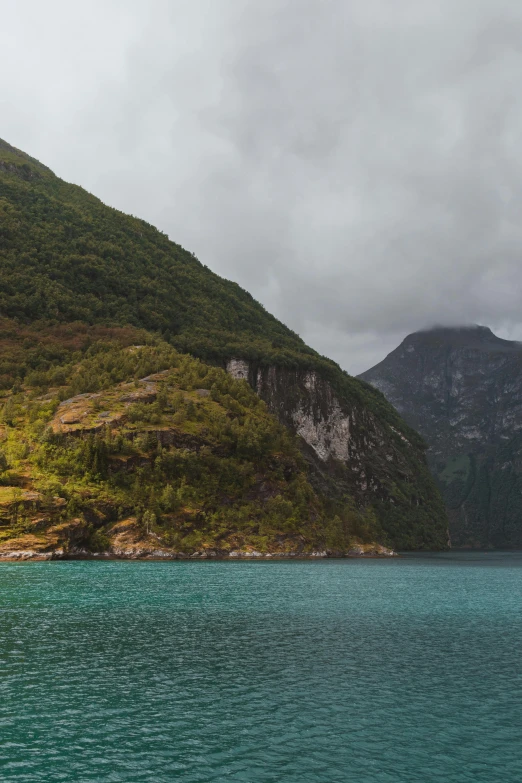 a body of water with a mountain in the background, fjords, coastal cliffs, dark green water, autumn