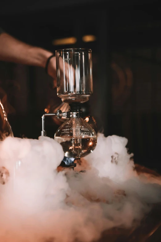 a glass filled with liquid sitting on top of a table, smoke machine, carefully crafted, mad scientist, cosy