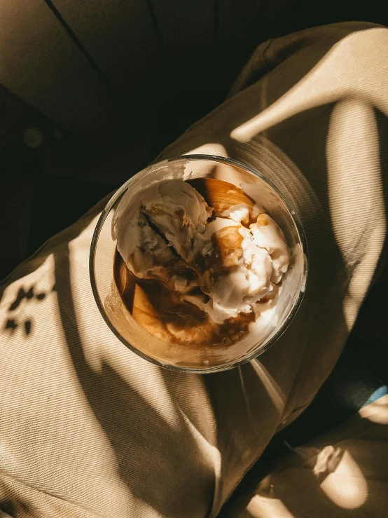 a glass of ice cream sitting on top of a pillow, inspired by Elsa Bleda, trending on unsplash, renaissance, gorgeous sunlight and shadows, maple syrup & hot fudge, 🎀 🧟 🍓 🧚, pov