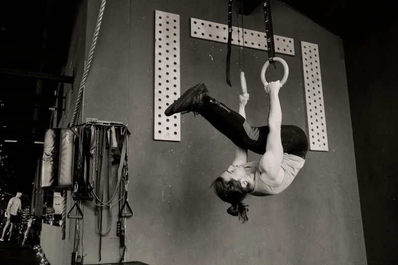 a black and white photo of a man hanging upside down, arabesque, rings, dingy gym, the empress’ hanging, square