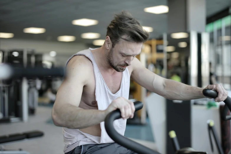 a man working out on a stationary bike in a gym, by Julian Allen, pexels contest winner, avatar image, sad expression, low quality photo, lachlan bailey